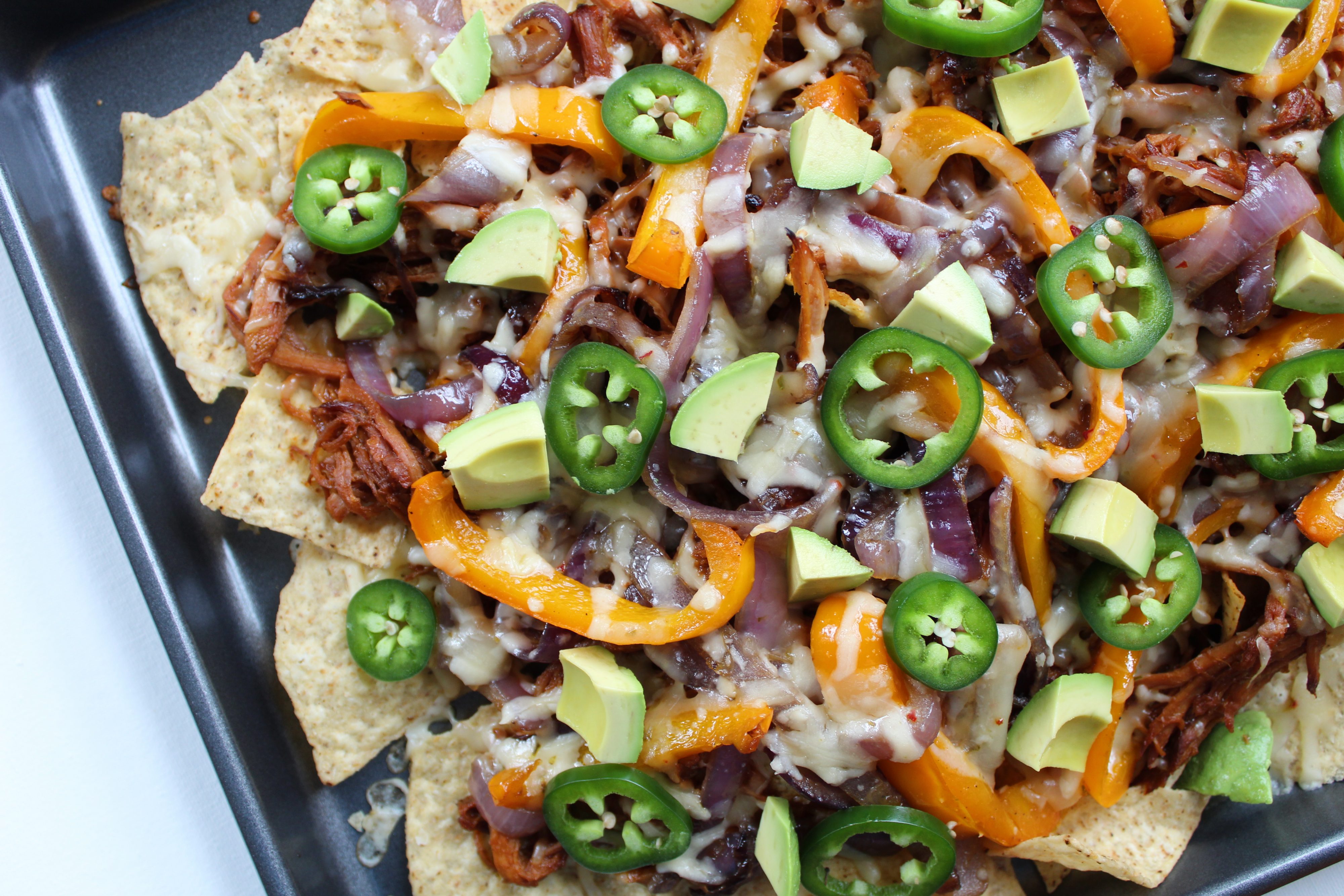 These nachos are topped with BBQ pork, fajita-style peppers and onions, and more fun toppings, and they'll make great party food!